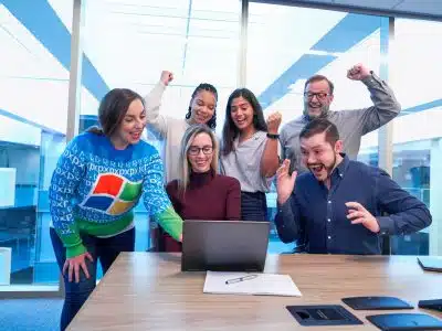 men and women sitting and standing by the table looking happy while staring at laptop